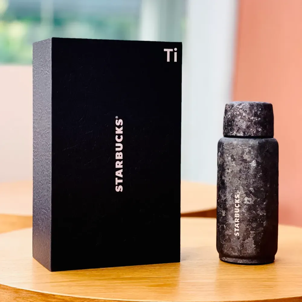 小型の1本は、正面に「STARBUCKS」、角に元素記号の「Ti」(チタン)だけを置いた黒箱に入る。本体は蓋まで同じ石目模様で覆われ、閉じると継ぎ目が見えにくい。ほかに茶こしと替えの蓋、ストラップをまとめた箱入りのギフトセットもある。