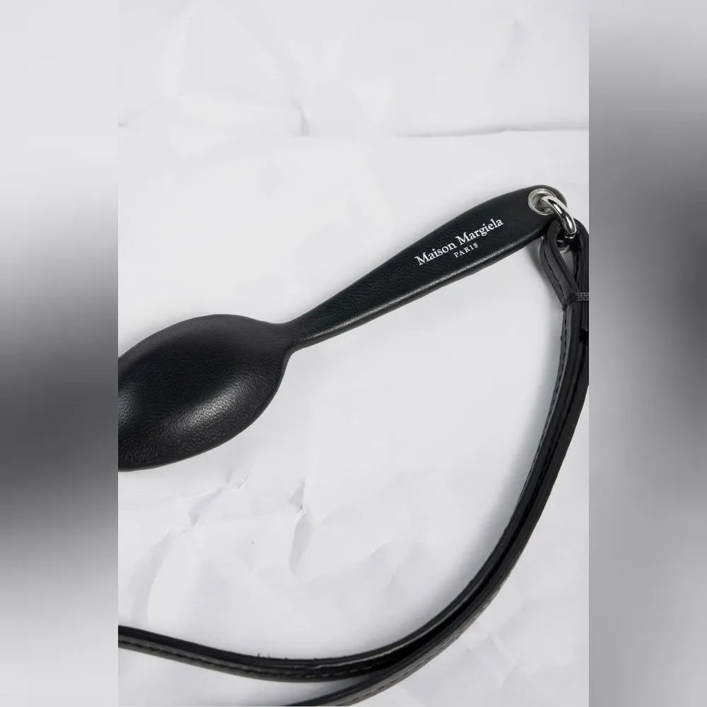持ち手には“Maison Margiela PARIS”のロゴをプリント。マットな黒のカーフレザーがスプーンの丸みに沿って張られ、食器のフォルムをそのまま革の小物に置き換えている。