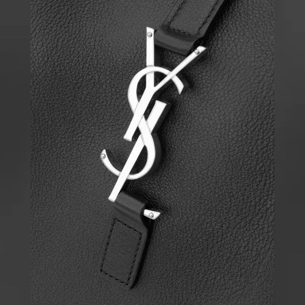 口はファスナーではなく、YSLモノグラムのフックをレザータブに掛けて留める。金具はシルバー調で、グレインの入ったカーフスキンの黒の上でロゴだけが光る。