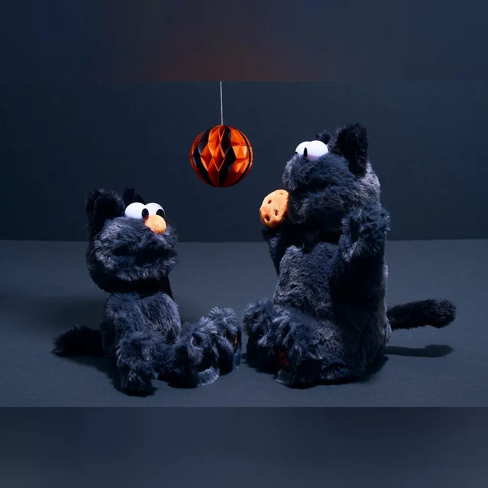 <p>ハロウィン限定のエルモとクッキーモンスターのぬいぐるみ。黒猫の仮装で、オレンジの鼻と足裏の刺繍がアクセント。ふわふわの手触りで、インテリアやギフトに最適。</p>